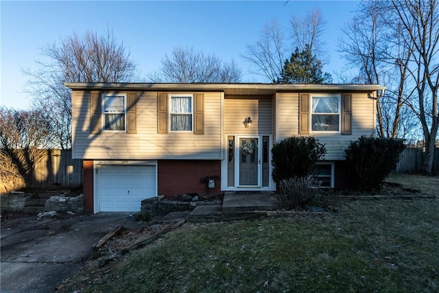 raised ranch with brick siding, an attached garage, fence, and driveway
