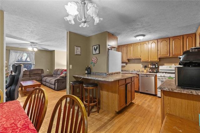 kitchen featuring ceiling fan with notable chandelier, a textured ceiling, white appliances, and light hardwood / wood-style flooring