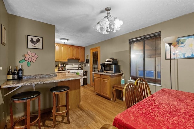 kitchen featuring white gas range oven, hanging light fixtures, a notable chandelier, light hardwood / wood-style floors, and kitchen peninsula