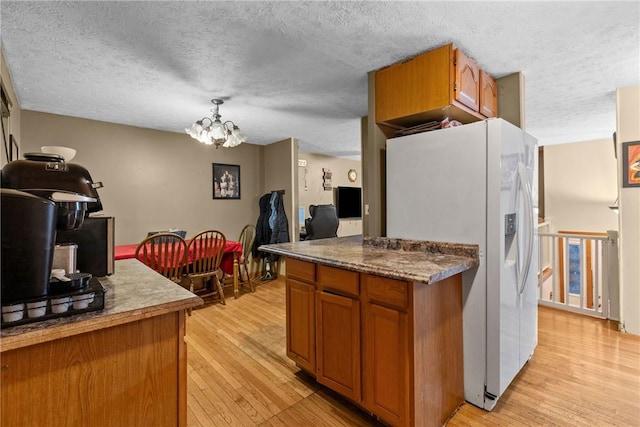 kitchen with light wood-type flooring, white fridge with ice dispenser, a chandelier, a textured ceiling, and brown cabinets