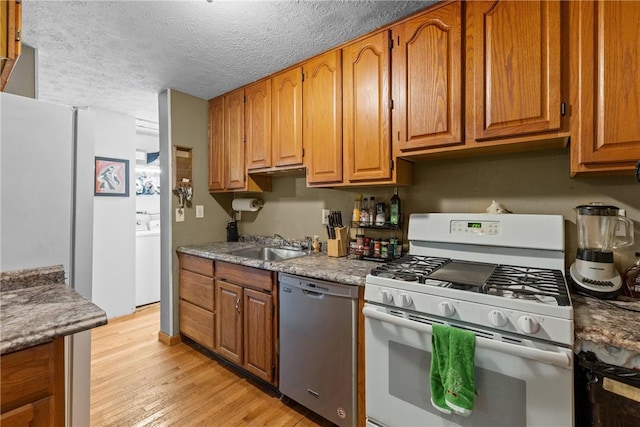 kitchen with dishwasher, light hardwood / wood-style flooring, washer / clothes dryer, a textured ceiling, and white range with gas cooktop