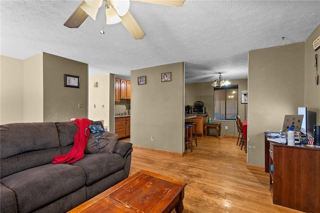 living room with ceiling fan with notable chandelier, a textured ceiling, and light wood-type flooring