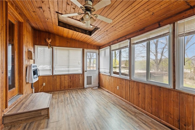unfurnished sunroom featuring heating unit, wood walls, lofted ceiling with skylight, wood ceiling, and wood finished floors