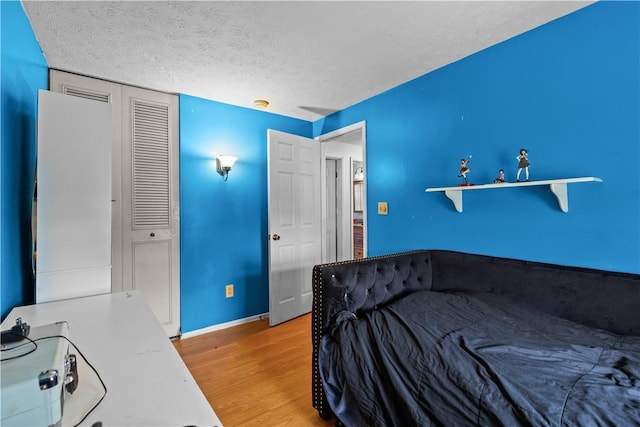 bedroom featuring a textured ceiling, wood finished floors, baseboards, and a closet