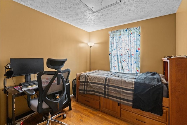 bedroom with a textured ceiling, wood finished floors, and attic access
