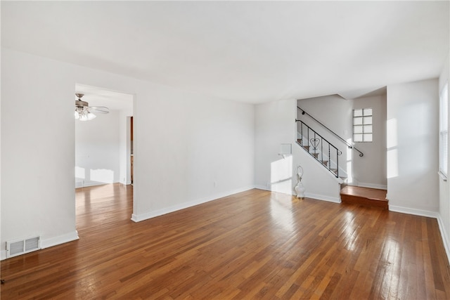 unfurnished room featuring baseboards, visible vents, hardwood / wood-style flooring, ceiling fan, and stairs