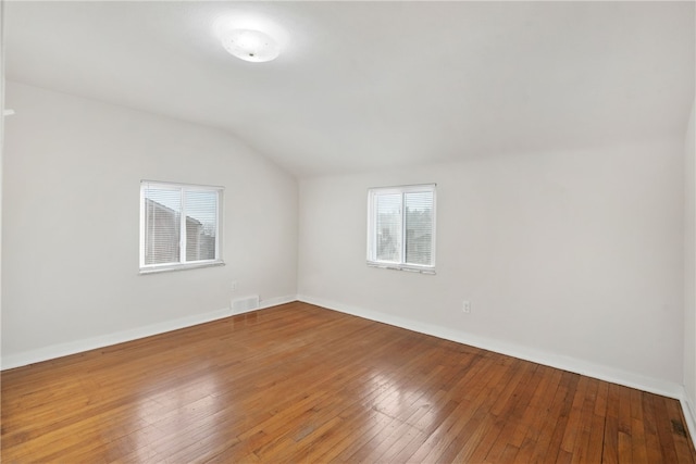 unfurnished room with lofted ceiling, wood-type flooring, visible vents, and baseboards