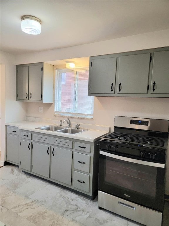 kitchen featuring marble finish floor, stainless steel gas stove, a sink, and gray cabinetry