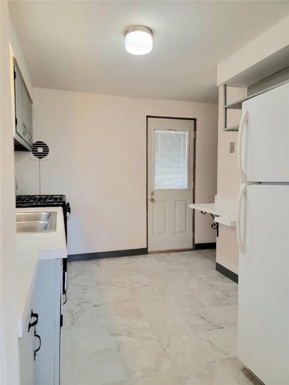 kitchen with baseboards, freestanding refrigerator, marble finish floor, light countertops, and a sink