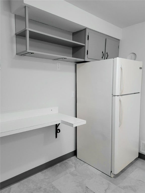 kitchen with marble finish floor, open shelves, gray cabinets, light countertops, and freestanding refrigerator