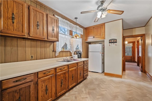 kitchen featuring sink, white refrigerator, wood walls, pendant lighting, and light parquet flooring