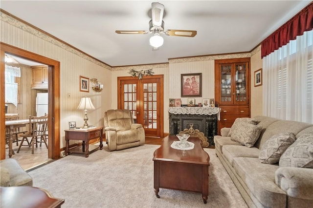 carpeted living room with a fireplace, ceiling fan, french doors, and crown molding