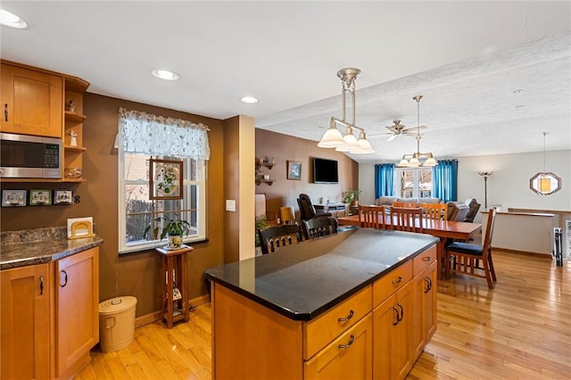 kitchen with pendant lighting, a center island, ceiling fan, dark stone countertops, and light hardwood / wood-style floors