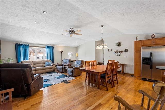 dining room featuring a textured ceiling, ceiling fan with notable chandelier, lofted ceiling, and light wood-type flooring