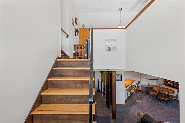 staircase with carpet flooring, crown molding, and an inviting chandelier