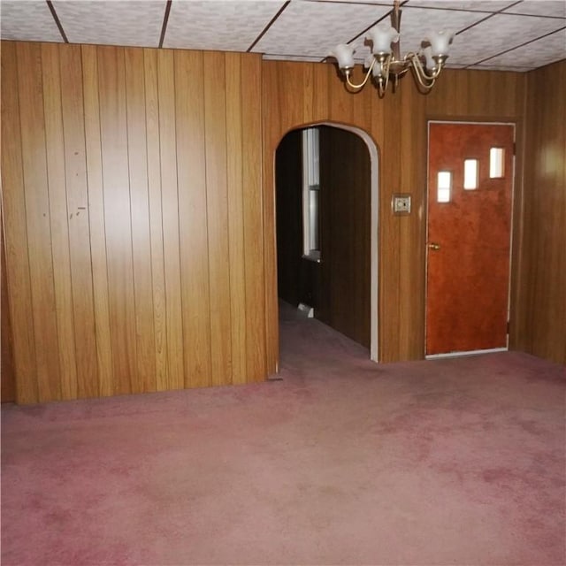 carpeted spare room featuring a chandelier and wooden walls