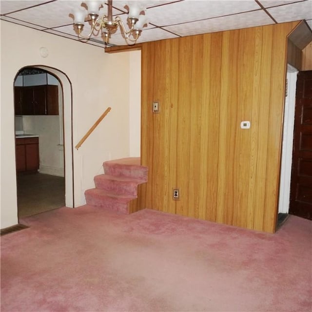 unfurnished room featuring carpet floors, an inviting chandelier, and wood walls