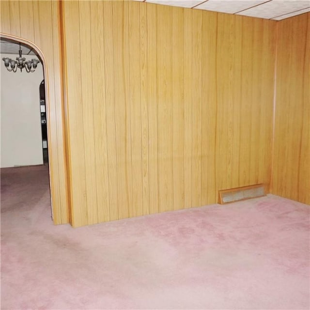 carpeted empty room featuring wood walls and an inviting chandelier