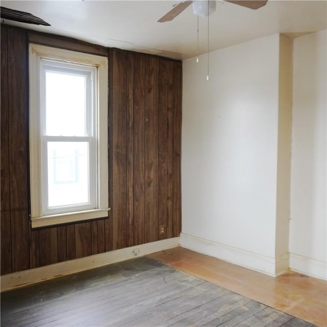 empty room with hardwood / wood-style flooring, ceiling fan, and wooden walls