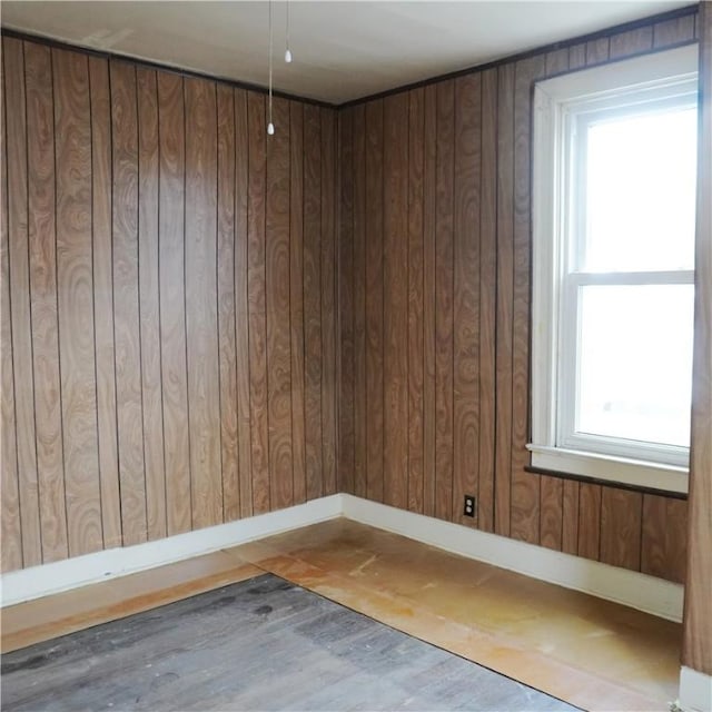 empty room with wooden walls, plenty of natural light, and wood-type flooring