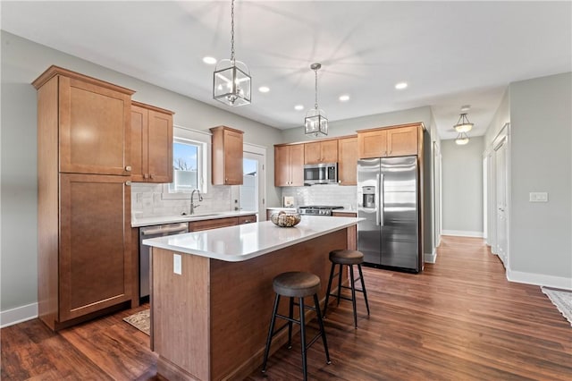 kitchen with pendant lighting, dark wood-type flooring, sink, appliances with stainless steel finishes, and a kitchen island