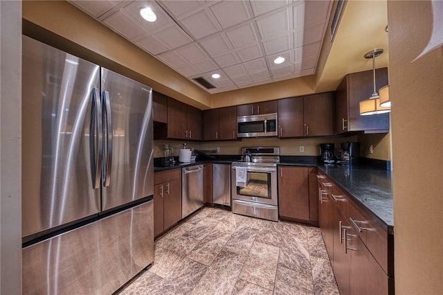 kitchen with appliances with stainless steel finishes, dark brown cabinetry, dark stone counters, and pendant lighting