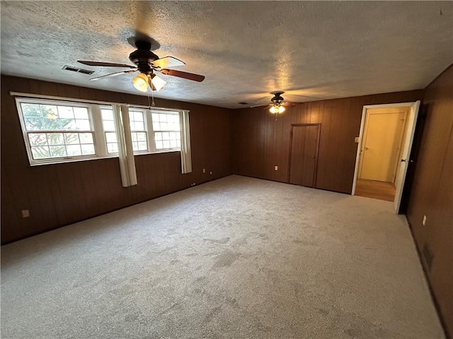 carpeted empty room with a textured ceiling, ceiling fan, and wood walls