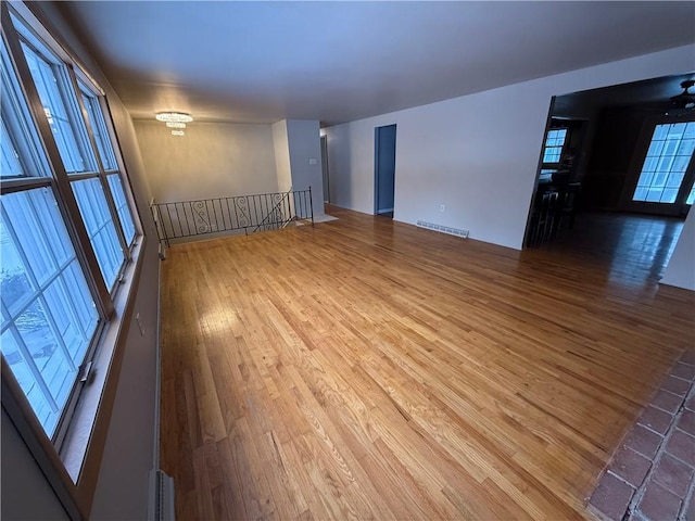 unfurnished room with an inviting chandelier, a wealth of natural light, and wood-type flooring