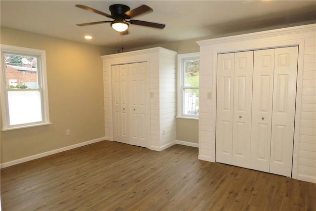 unfurnished bedroom with dark hardwood / wood-style floors, ceiling fan, two closets, and multiple windows