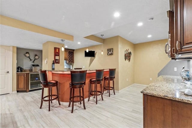 bar with wine cooler, light stone counters, hanging light fixtures, and light hardwood / wood-style floors