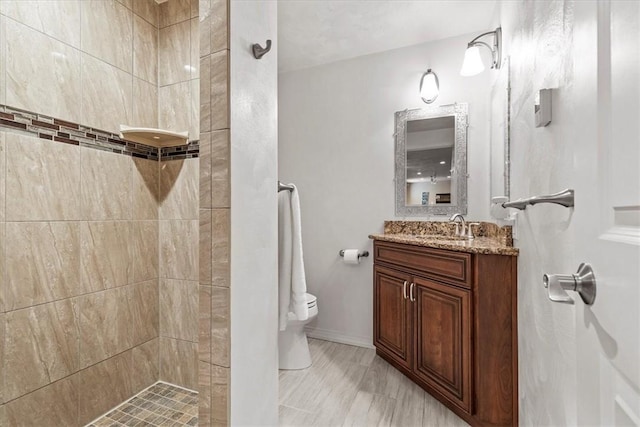 bathroom with a tile shower, vanity, and toilet