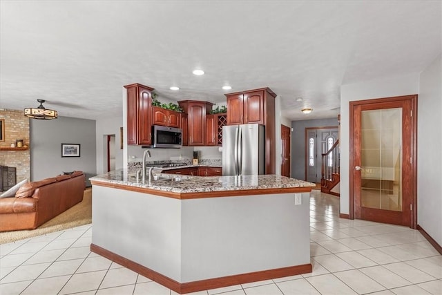 kitchen with light tile patterned floors, a peninsula, a sink, appliances with stainless steel finishes, and a brick fireplace