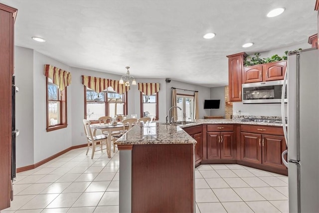 kitchen with light tile patterned floors, a peninsula, a sink, appliances with stainless steel finishes, and light stone countertops