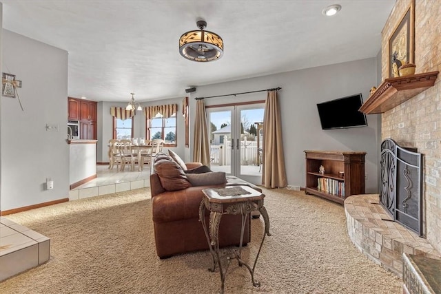 carpeted living room featuring a brick fireplace, french doors, and an inviting chandelier