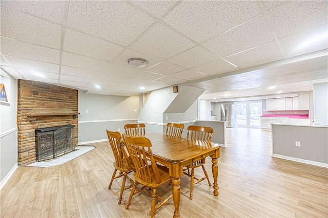 dining room with light wood-type flooring, a stone fireplace, and a drop ceiling