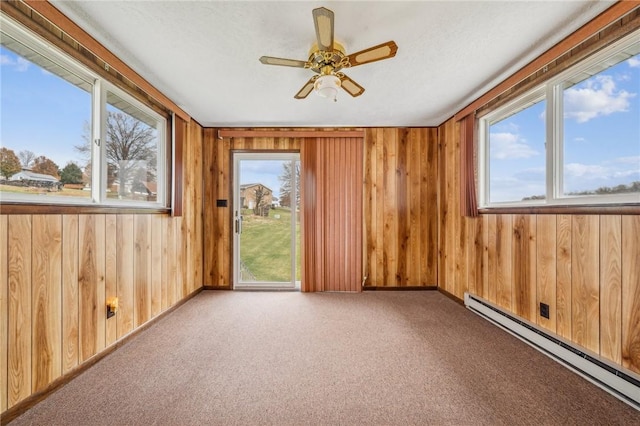 unfurnished room featuring a baseboard radiator, ceiling fan, light colored carpet, and wood walls