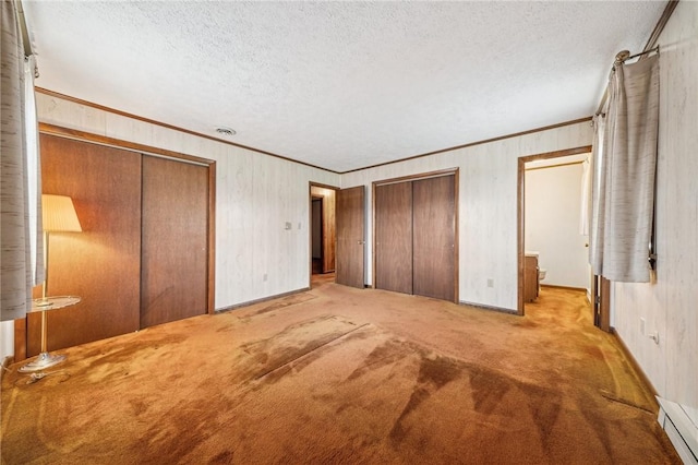 unfurnished bedroom with light carpet, a textured ceiling, crown molding, a baseboard heating unit, and multiple closets