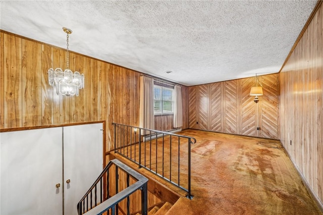 interior space featuring carpet, a textured ceiling, an inviting chandelier, and wood walls