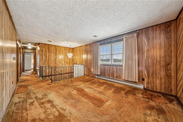 empty room with carpet flooring, wood walls, a textured ceiling, and a baseboard heating unit