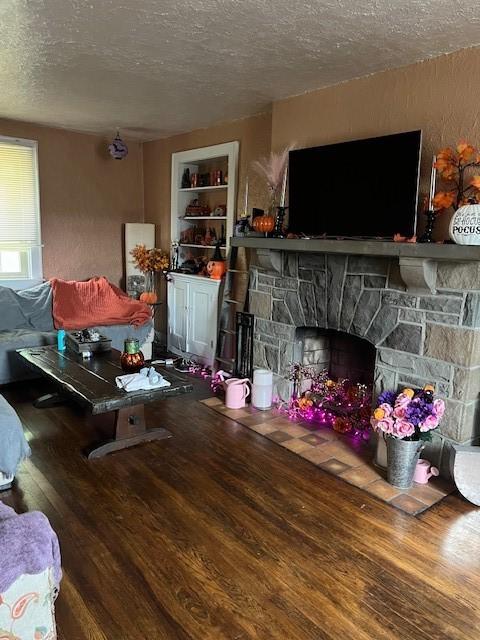 living room with hardwood / wood-style floors, a stone fireplace, built in features, and a textured ceiling