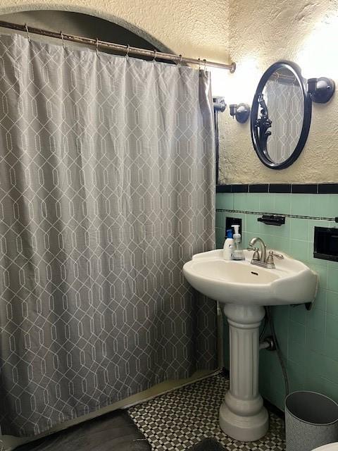 bathroom with a textured ceiling, curtained shower, and tile walls