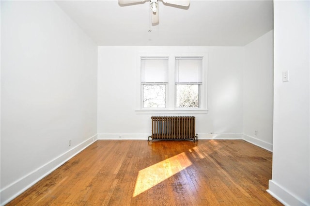 spare room featuring ceiling fan, wood-type flooring, and radiator heating unit