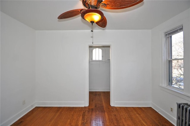 empty room with dark hardwood / wood-style floors, ceiling fan, and radiator