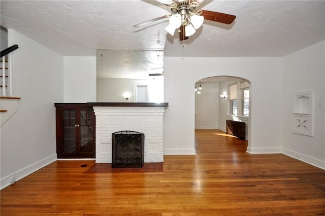 unfurnished living room with ceiling fan, wood-type flooring, a textured ceiling, and a brick fireplace