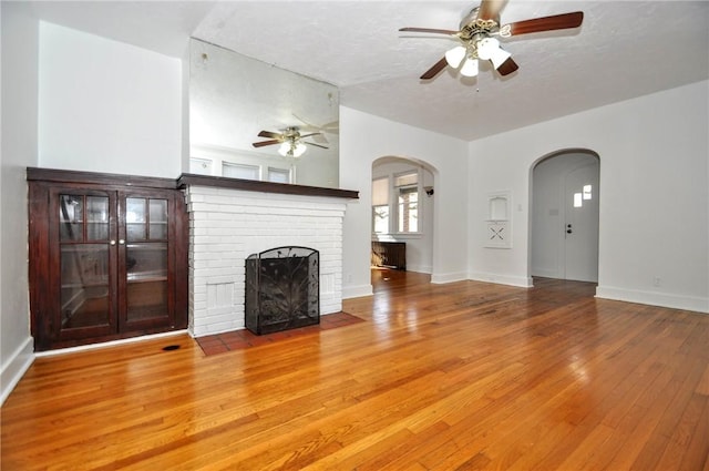 unfurnished living room with a brick fireplace, ceiling fan, a textured ceiling, and hardwood / wood-style flooring