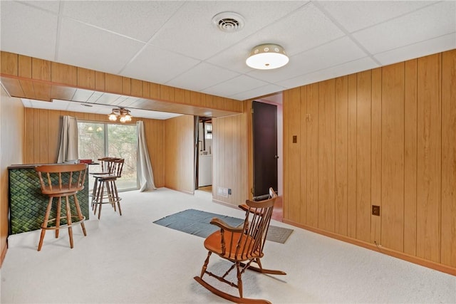 living area featuring light carpet, a drop ceiling, and wooden walls