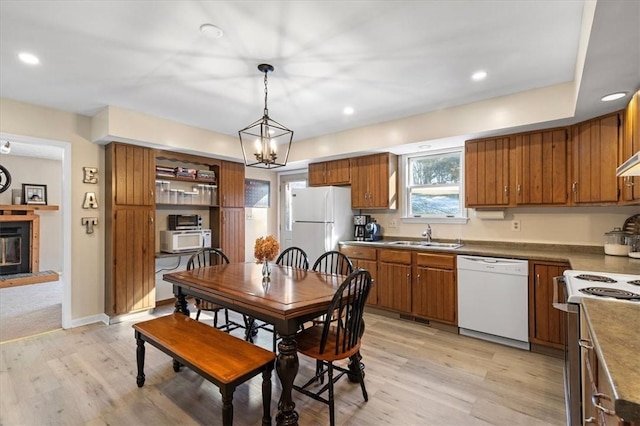 kitchen with pendant lighting, white appliances, sink, light wood-type flooring, and a chandelier