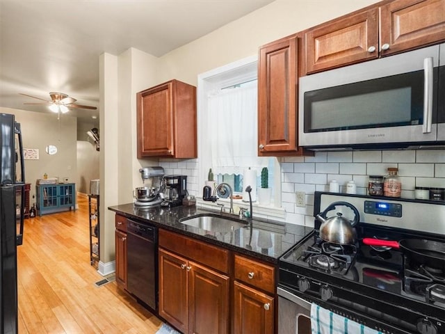 kitchen with decorative backsplash, stainless steel appliances, sink, dark stone countertops, and light hardwood / wood-style floors