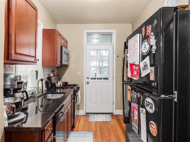 kitchen with decorative backsplash, appliances with stainless steel finishes, dark stone counters, sink, and light hardwood / wood-style floors