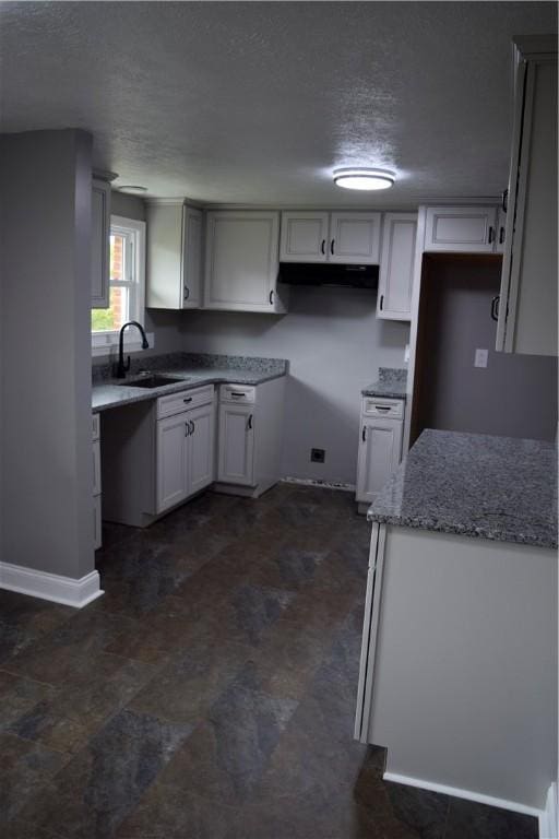 kitchen with white cabinets, light stone counters, sink, and a textured ceiling